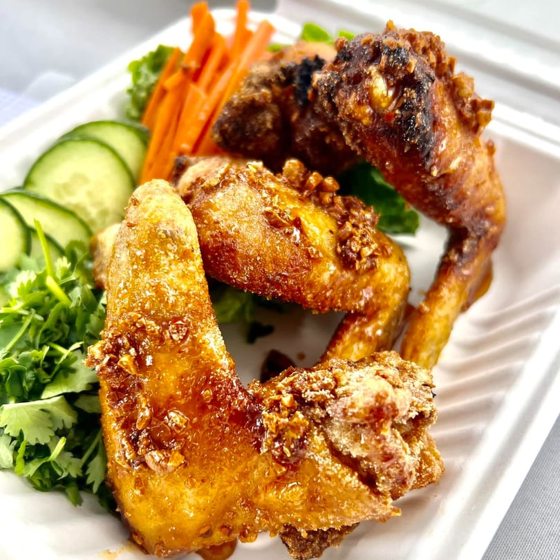 Fyre Wings' crispy, golden-brown wings with garlic bits, served with fresh cucumber, carrots, and cilantro.