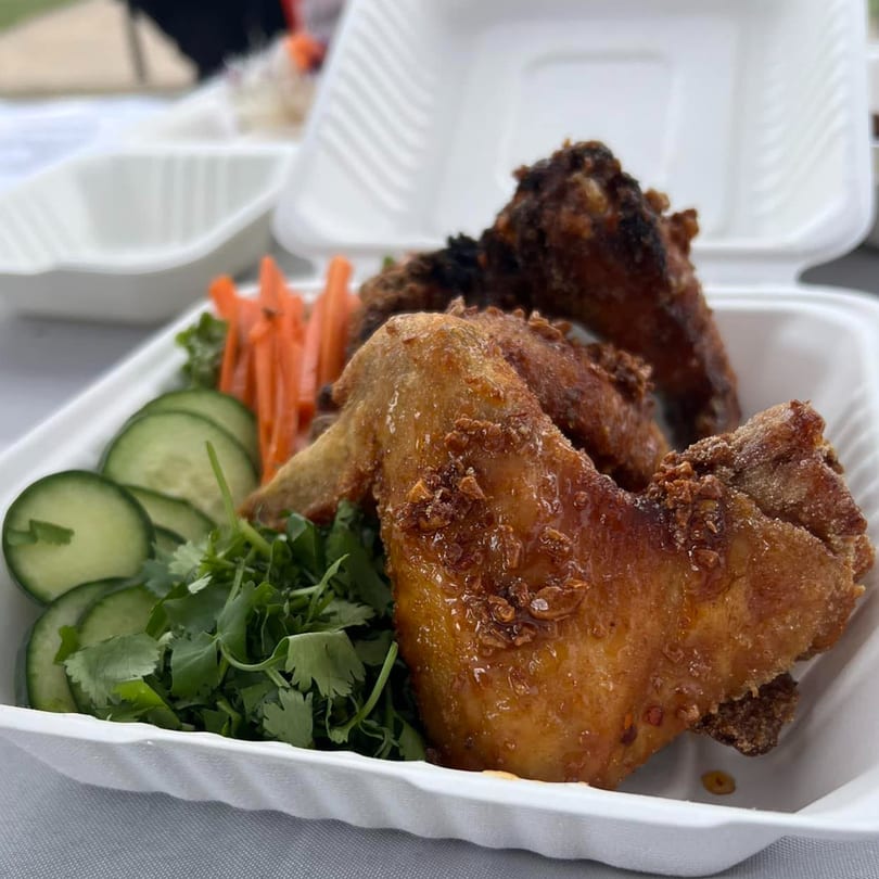 Crispy Fyre Wings with fresh cilantro, cucumber slices, and shredded carrots in a takeout container.