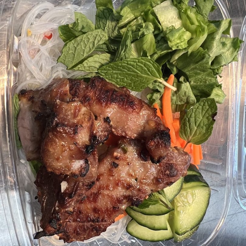 Grilled meat with vermicelli noodles, lettuce, carrots, mint, and cucumber in a clear container.