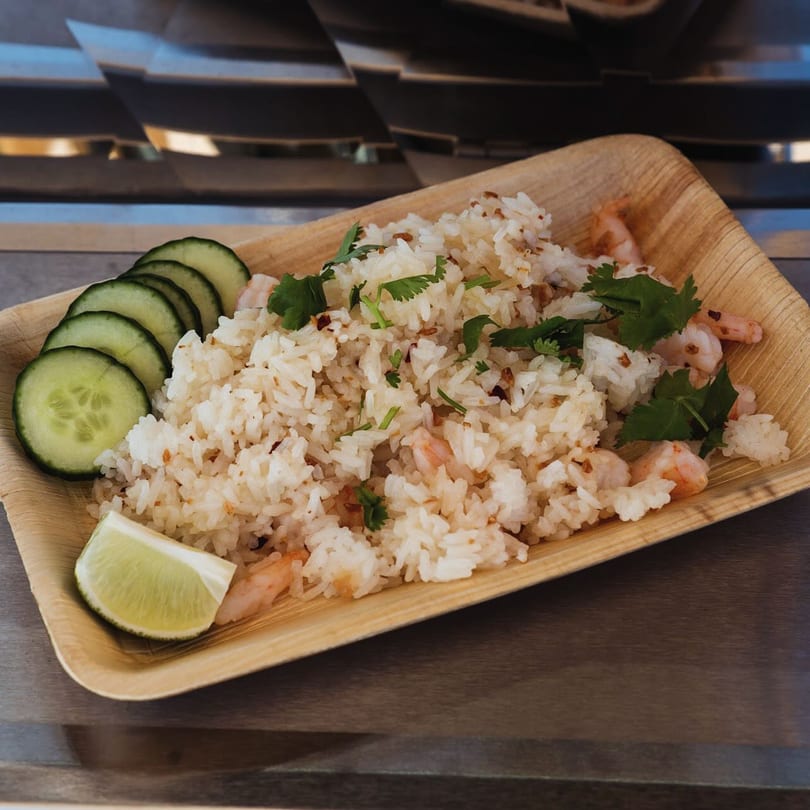 Shrimp fried rice with cilantro, cucumber slices, and a lime wedge on a wooden plate.